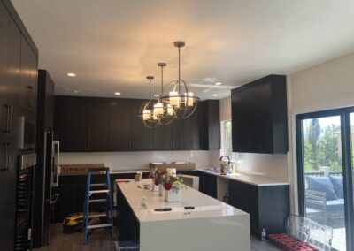 Modern kitchen with dark cabinets, white countertops, and three pendant lights above the island; tools and supplies indicate ongoing installation or renovation.