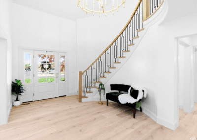 A spacious foyer with light wood floors, a curved staircase with black railings, a green velvet bench, a potted plant, and a large chandelier.